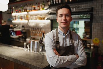 Fototapeta premium portrait of a staff member waiter in a restaurant cafe bistro. a young man of European appearance is waiting for new satisfied customers for dinner. professional work wear apron and shirt