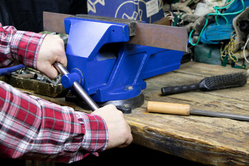 Blue vise on a wooden table. Bench tools. Vice. Men's hands hold a vise. A locksmith vise