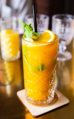 sea buckthorn cocktail with mint in a crystal glass on a table in a bar