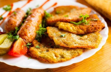 potato pancakes with fried sausages on a white plate