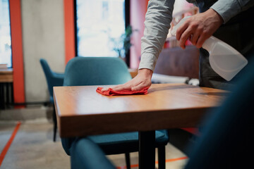 disinfection antibacterial cleaning of the virus in a cozy little cafe. the waiter wipes and cleans the table with a special anti-virus agent against the bacteria of the coronavirus pandemic.