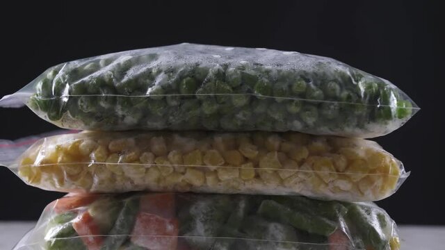 Rotating plastic bags with frozen vegetables on dark background, closeup