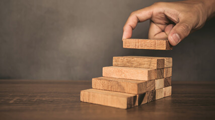 Close-up hand is placing wood block tower stacked in pyramid shape with caution to prevent collapse...