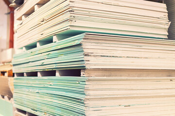 Pallet with Drywall sheets plasterboard in the building warehouse store. Stacking of white gypsum panels, drywall or plasterboard. Gypsum plasterboard in the pack. toned