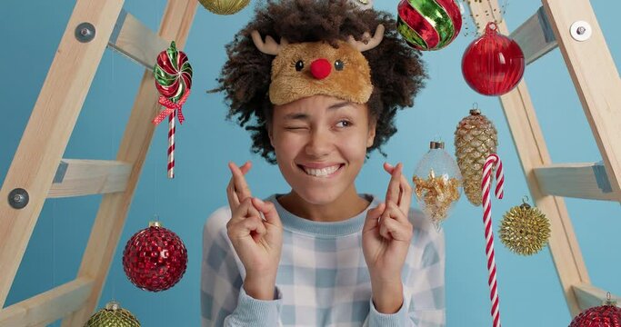 Christmas wish concept. Happy young curly Afro American woman hopes for dreams come true crosses fingers and prays for better life celebrates New Year at home surrounded by holiday decorations