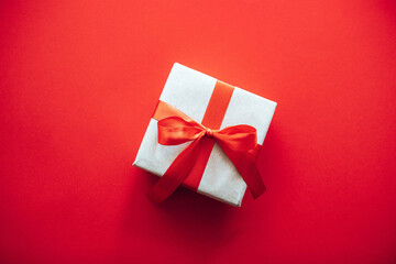 Gift box wrapped in craft paper with red ribbon bow and copyspace on red background. Top view composition