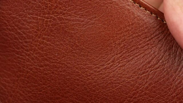 human finger testing texture of brown or red natural smooth matt luxury leather, check quality of fashion accessories material, cognac or brandy color, close-up macro view