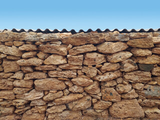 Irregular granite stone wall with veneer top layer under clear blue sky. Decorative brick fence wall against blue sky.