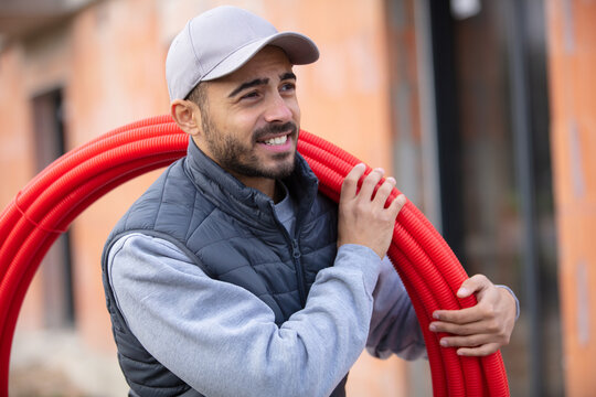 male builder carrying reel of red pipe on shoulder