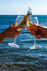 splash of champagne or white wine from glass against background of ocean. two glasses. celebration or romantic date