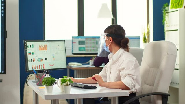Coworkers with protection face masks working together in workplace during pandemic. Team in new normal business financial office typing on computer, checking reports, analysing data looking at desktop - Powered by Adobe