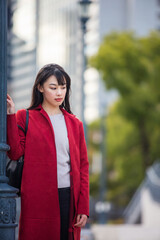 Fototapeta premium 赤いコートを着た都心で働く長い髪の若い女性