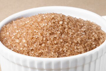 Brown refined sugar in a bowl on a beige background. Cane sugar