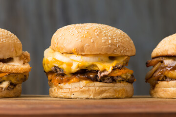 set of three hamburgers with bacon caramelized onion and breaded onion on white bread with sesame seeds