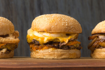 set of three hamburgers with bacon caramelized onion and breaded onion on white bread with sesame seeds