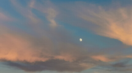Fototapeta na wymiar Luna piena al tramonto in un cielo azzurro con nuvole colorate