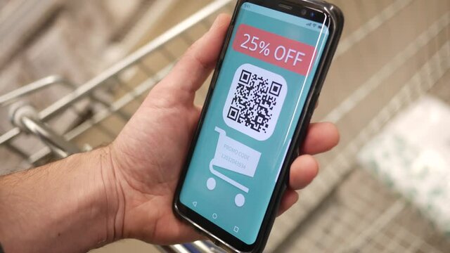 Holding a digital discount coupon on a mobile phone at a store. The coupon has a QR code ready to be scanned by the cashier.