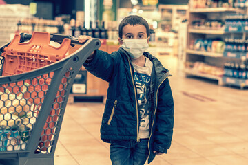 Obraz premium Boy wears protected mask in store. Shopping time during coronavirus outbreak. Boy in a medical mask. Shopping with kids during virus outbreak. Boy in face mask in supermarket. toned