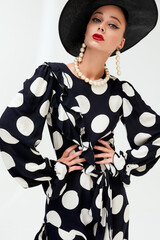 Woman with black hat wide and polka dot dress posing for fashion on a white background vertical photos - 396099604