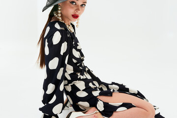 Woman with black hat wide and polka dot dress posing for fashion on a white background vertical...