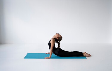 Young woman practicing yoga, lying and stretching in Cobra pose, doing Bhujangasana exercise. Attractive girl in black sportswear. Beautiful sporty fit yogini woman practices yoga asana bhujangasana.