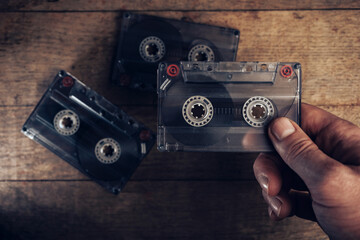 Hand holding audio cassette tape on brown old wooden table. Minimalism retro style concept....