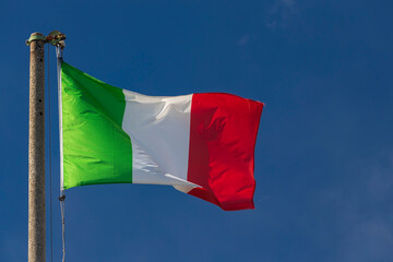 Naklejka na ściany i meble Italian flag blowing in the wind in the blue sky