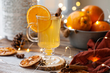 Delicious hot winter drink in glass mug: spicy tea with cinnamon, anise, orange. Citrus is a natural antiviral remedy. Cozy home holiday atmospehere with christmas lights on background.  Close up
