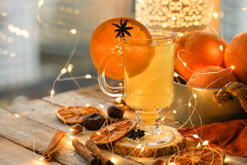 Delicious hot winter drink in glass mug: spicy tea with cinnamon, anise, orange. Citrus is a natural antiviral remedy. Cozy home holiday atmospehere with christmas lights on background.  Close up
