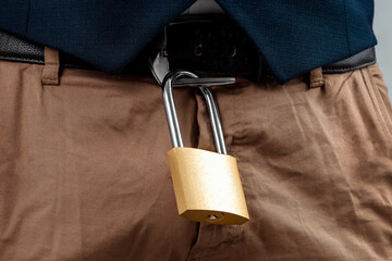 Close-up of a gold padlock hanging from a man's belt. The concept of marital fidelity, celibacy,...