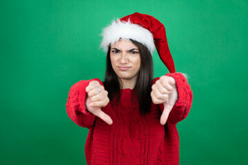 Young beautiful woman wearing Christmas Santa hat over isolated green background with angry face,...