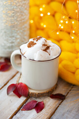 Delicious drink for cold autumn days: hot chocolate or latte with whipped cream and cinnamon. Cozy calm home atmosphere of lazy weekend morning. Yellow plaid and wooden table on background.