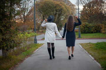 Girls hold hands. Two women are walking down the street. Shooting from the back. Walk in the park.