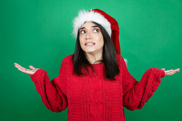 Young beautiful woman wearing Christmas Santa hat over isolated green background clueless and...