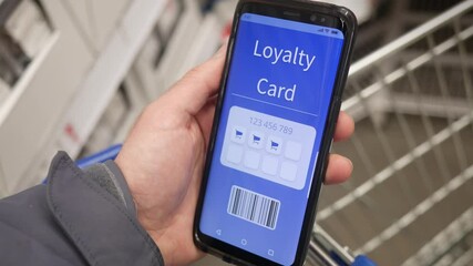 Holding a mobile phone with a loyalty card on the screen at a store to collect rewards and rebates.