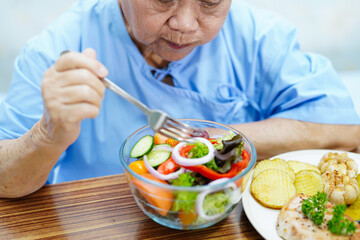 Asian senior or elderly old lady woman patient eating breakfast vegetable healthy food with hope and happy while sitting and hungry on bed in hospital.