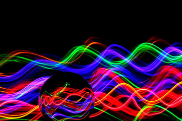 Long exposure photograph of neon multi colour in an abstract swirl, parallel lines pattern against a black background with reflections in a glass crystal ball. Light painting photography.
