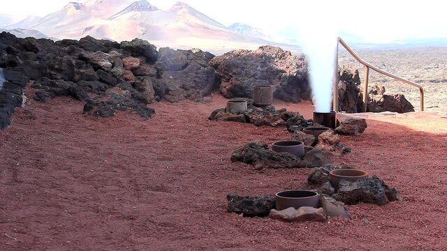 Man pouring bucket of water into geyser and steam erupts abruptly in Timanfaya National Park. Tourist attraction, geothermal phenomenom concepts
