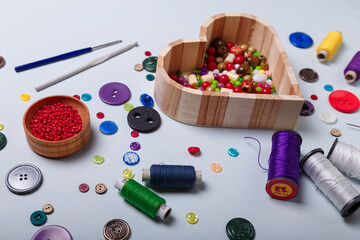 Close up of wooden heart shaped box of multicolored beads and buttons, awl, scissors, crochets and...