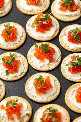 Salmon caviar and soft cheese savory crackers with sesame and poppy seeds served on black slate board