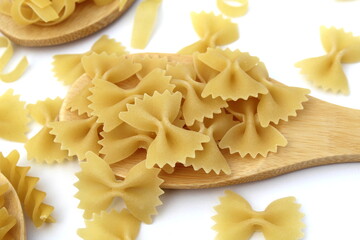 Obraz na płótnie Canvas Pasta in the form of bows lie on a wooden spoon on a white background