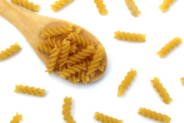 Pasta in the form of a spiral lie on a wooden spoon on a white background