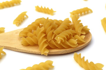 Pasta in the form of a spiral lie on a wooden spoon on a white background