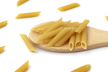 Pasta in the form of pipes lies on a wooden spoon on a white background