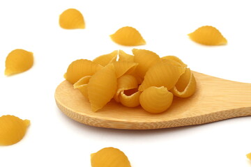 Pasta in the form of a shell lie on a wooden spoon on a white background