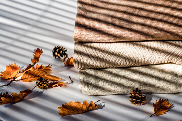 Autumn and winter season knitwear, leafs and fir cones with shadows on white background.