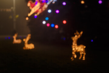 Unfocused night shot of Christmas reindeers and garland lights bokeh in the city. Happy New Year, Merry Christmas, winter holidays concept.