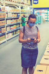 Woman wearing face mask and shopping in grocery store. Concept of protection against coronavirus and communication. Adult woman in medical mask using smartphone and shopping for groceries. toned