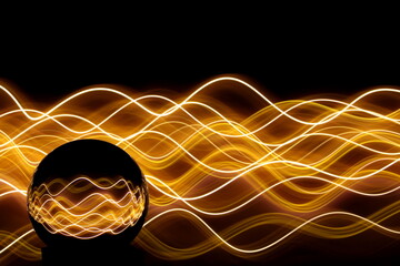 Long exposure photograph of neon gold colour in an abstract swirl, parallel lines pattern against a black background with reflections in a glass crystal ball. Light painting photography.