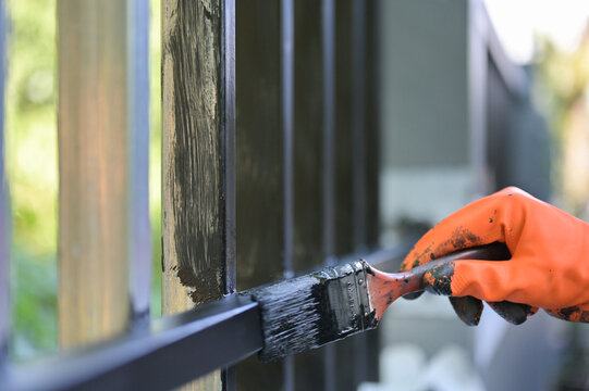 Worker painting steel with paint brush and orange gloves selective focus on hand